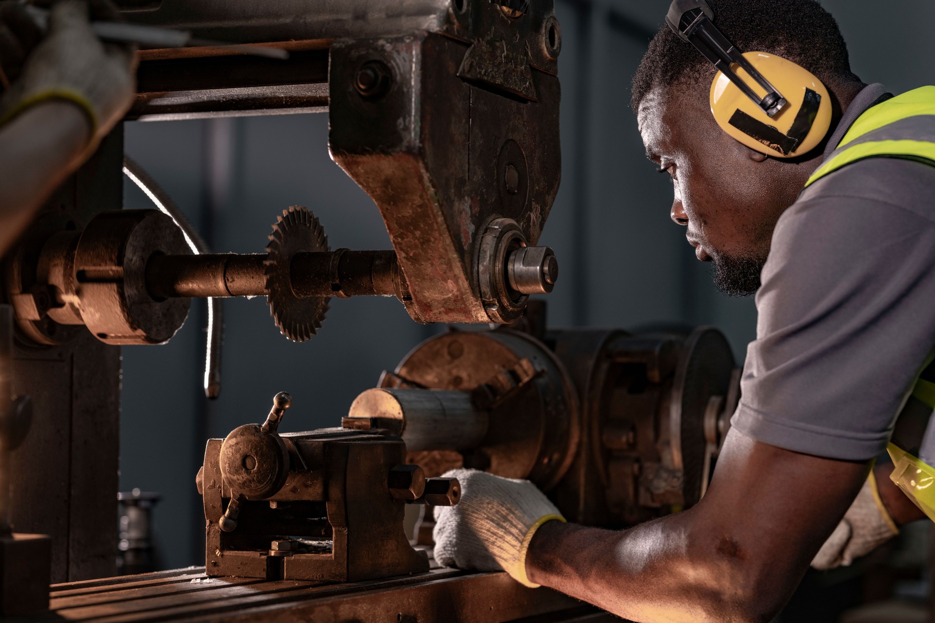 Focused industrial technician operating heavy machinery with precision. Wearing ear protection and safety gear, the professional works in a brightly lit workshop, emphasizing safety and expertise.